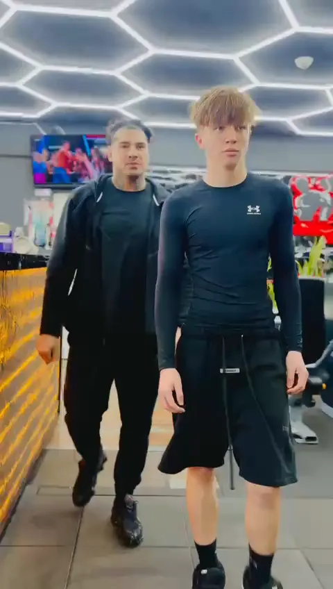 Antrenorul și un sportiv adolescent la o sesiune de forță într-o sală de fitness: ridicări pe vârfuri cu bară, scăriță de agilitate, alergare cu sac pe umeri. Clip montat, cu text scris peste imagine.